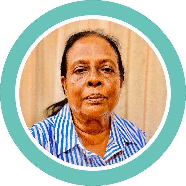 A photograph of Muthukuda (Sarojini) Goonetilleke, a Foothold community member who applied for financial support. Sarojini is looking towards the camera. The photo is is surrounded by a branded teal circle.