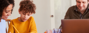 A family consisting or a man, woman and boy sitting at a table. Representing an IET member renewing his IET membership, the man is working on a laptop, whilst the woman and boy are doing a crafting activity together.