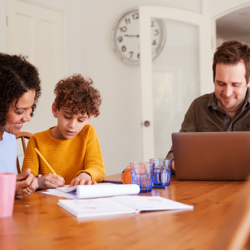 A family consisting or a man, woman and boy sitting at a table. Representing an IET member renewing his IET membership, the man is working on a laptop, whilst the woman and boy are doing a crafting activity together.