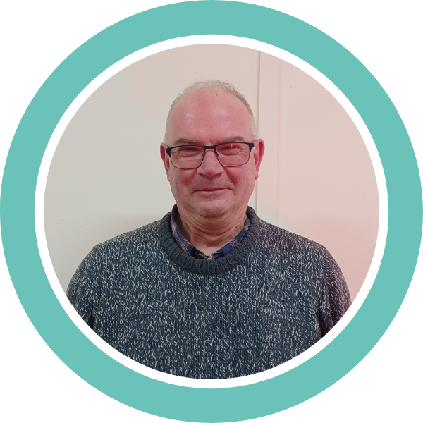 A photo of Adam wearing a grey jumper and glasses, smiling, within a teal coloured circle